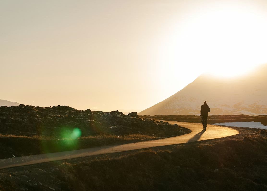 A lone figure walking a winding path toward the sunrise